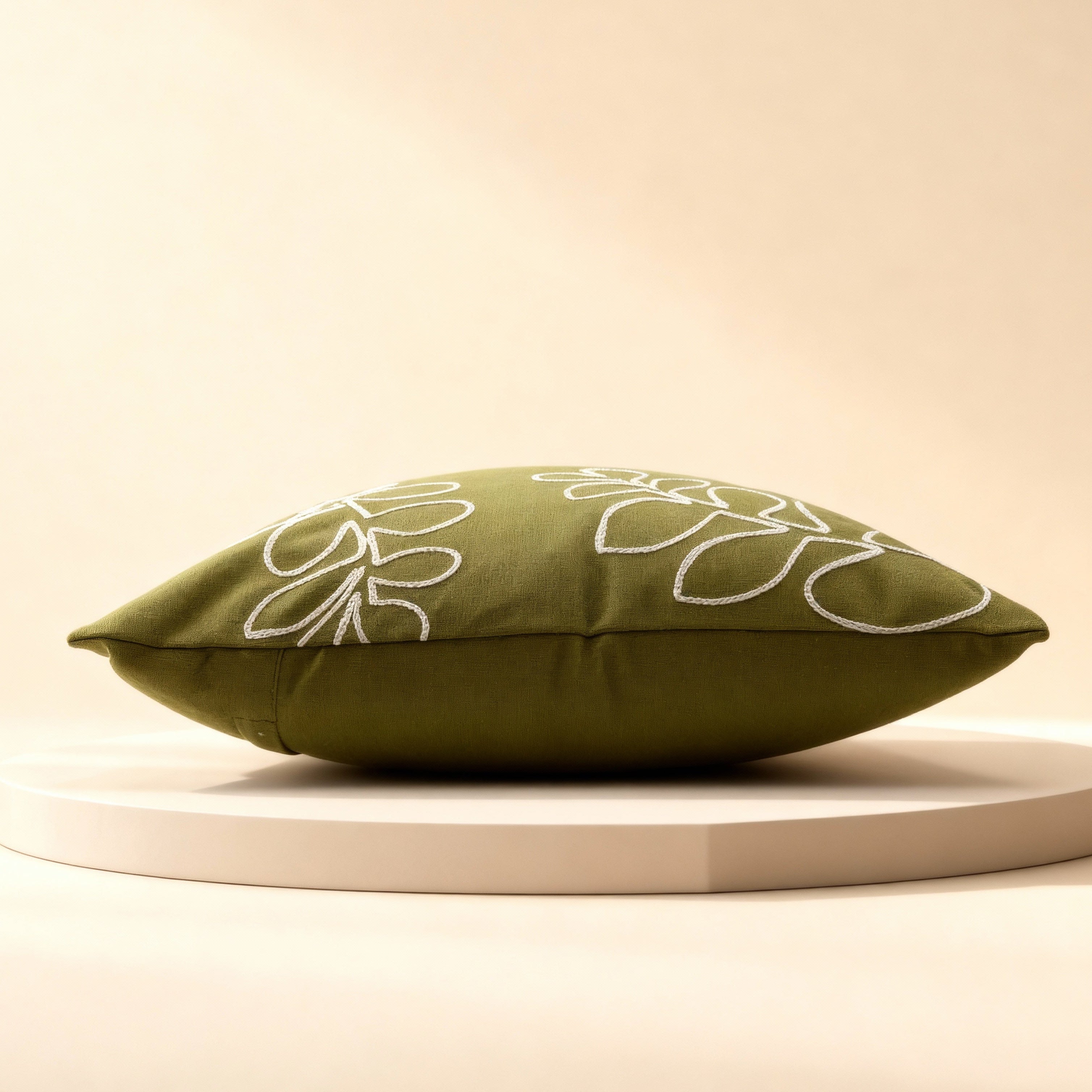 Green pillow with white floral patterns on a beige platform against a beige background